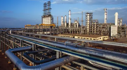 A large industrial oil refinery with extensive pipelines and metal structures under a blue sky.