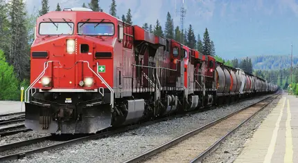 A red freight train transporting cargo containers as it moves through a rural landscape on railway tracks.